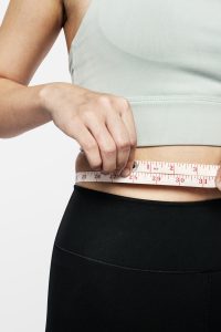 Mujer midiendo su perímetro abdominal con una cinta métrica para controlar cambios corporales.